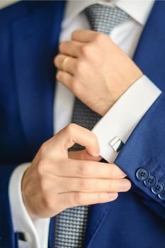 Groom or businessman fasten cufflink on the cuff of the shirt wearing blue suit