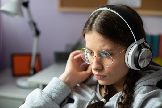 A brunette girl listens intently to a new song by her favorite music band. A young girl with braids and glasses listens to music.