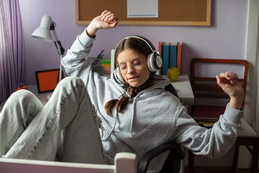 A teen raises her hands while listening to music. Musical emotion is translated into verbal emotion. A young girl with braids and glasses listens to music.