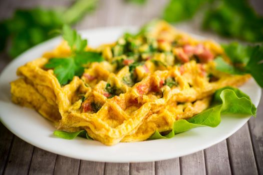 Egg omelet stuffed with greens and sausage fried in the form of waffles, on a wooden table