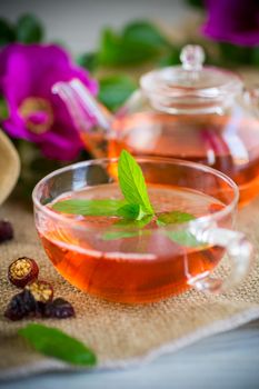 brewed rosehip tea in a glass teapot with rosehip flowers and mint, on a wooden table.