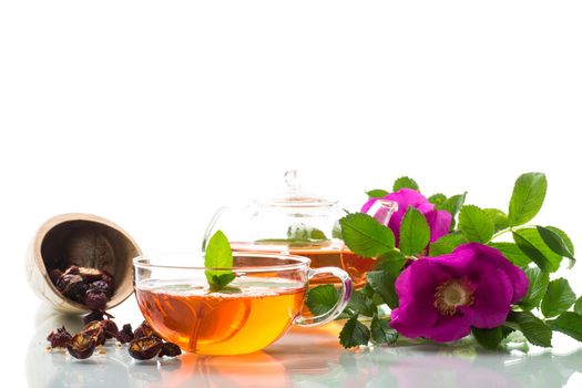 brewed rosehip tea in a glass teapot with rosehip flowers and mint, isolated on white background.