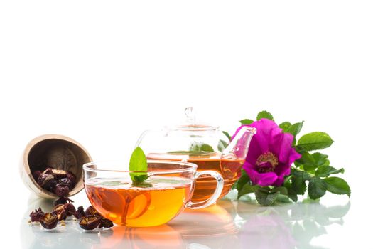 brewed rosehip tea in a glass teapot with rosehip flowers and mint, isolated on white background.