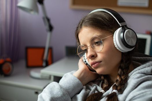 A teenage girl listens to music on headphones with complete seriousness. Young girl in pigtails and glasses concerned during music message.