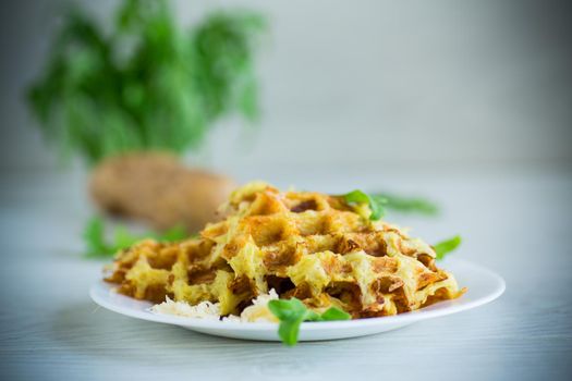 fried potato waffles with cheese in a plate on a light wooden table.