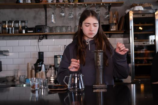 pretty brunette girl making aeropress coffee in modern coffee shop.