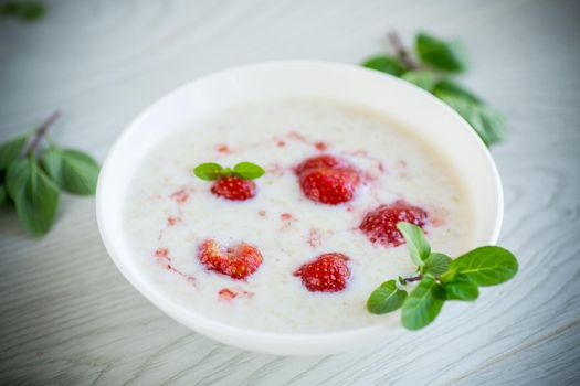 sweet milk oatmeal with strawberries in a plate, on a wooden table.