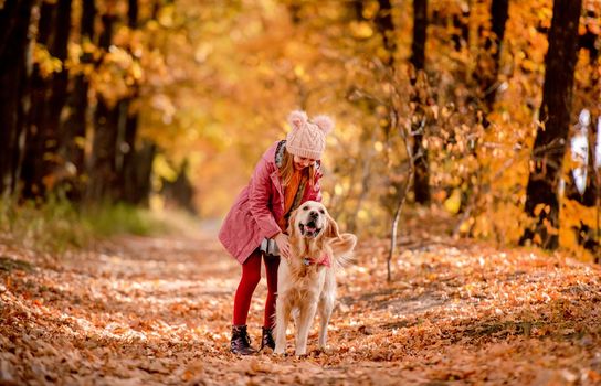Preteen girl kid petting golden retriever dog at autumn park and smiling. Beautiful portrait of child and pet doggy outdoors at nature