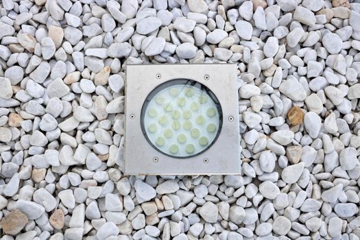 Built-in modern round-shaped lamp on white gravel in the garden.