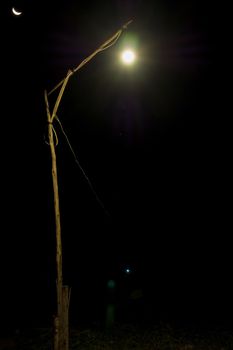 Lighting from bulb at the end of old wood pole and light from crescent moon in the dark night