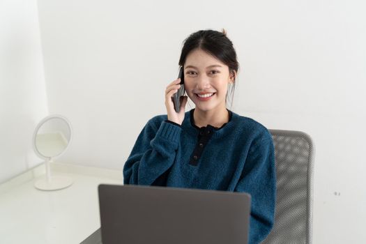 Portrait of smiling beautiful business asian woman using laptop computer and calling byh mobile phone from home concept.