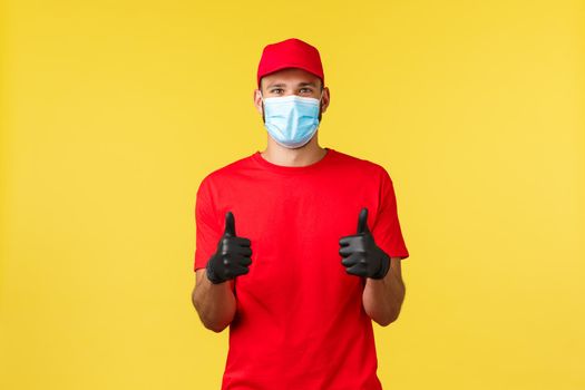 Express delivery during pandemic, covid-19, safe shipping, online shopping concept. Courier approves and agrees, wear red uniform, medical mask showing thumbs-up, recommend shipping promo.