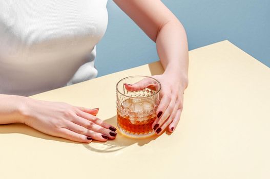 Glass with Whiskey and Ice Cube in Woman Hands on Table on Blue Background. Modern Isometric Style. Creative Concept.