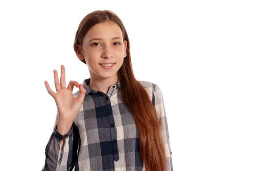 Portrait of an attractive teenage female in a casual checkered shirt showing ok sign and smiling while posing isolated on white studio background. Long hair, healthy clean skin and brown eyes. Sincere emotions concept. Copy space.