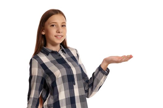 Portrait of a lovely teenage female in a casual checkered shirt acting like holding something in her hand and looking at the camera while posing isolated on white studio background. Long hair, healthy clean skin and brown eyes. Sincere emotions concept. Copy space.