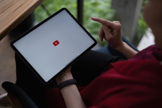 Chiang mai, Thailand - AUG 09, 2021 : Woman using a tablet to connect to YouTube Premium. YouTube is a video-sharing website by google.