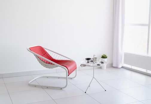 Minimal light and airy interior. White living room with red leather chair and coffee table