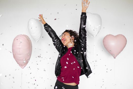 The emotion of success. Happy sexy brunette girl enjoying celebrating with confetti and heart balloons on a white background.