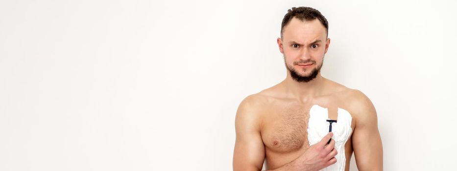 Young caucasian man with beard holds razor shaves his chest with white shaving foam on white background. Man shaving his torso