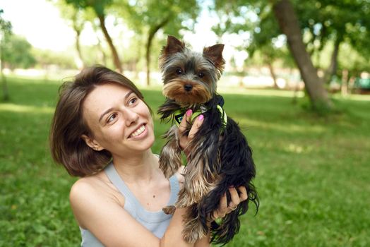 A cute girl with a square hugs a Yorkshire terrier on the street. Hugs with your little dog in the park.