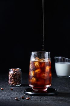 Iced Coffee Pouring into Tall Glass on Dark Background. Concept Refreshing Summer Drink.