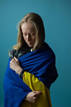A real Ukrainian blonde woman during the war with the state yellow and blue Ukrainian flag on her head. Russia attacked Ukraine on February 24, 2022.