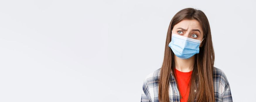 Coronavirus outbreak, leisure on quarantine, social distancing and emotions concept. Thoughtful and intrigued woman in medical mask, looking left with interest, thinking, white background.