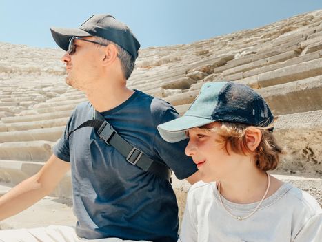 Young father dad and his school boy kid son tourists visiting ancient antique coliseum amphitheater ruins in hot summer day.