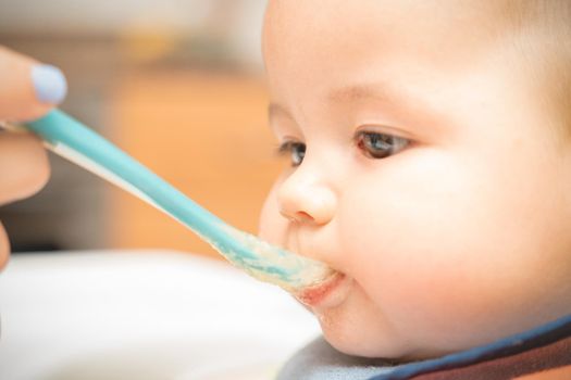 Cheerful baby child eats food with spoon. Portrait of happy kid boy in high chair. High quality photo