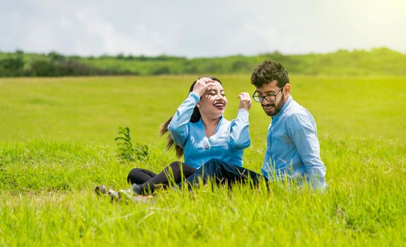 A couple in love sitting in the field, Romantic couple sitting on the grass outdoors, Smiling teenage couple sitting on the grass on a sunny day