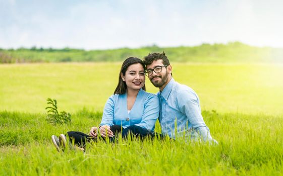 Young couple in love sitting on the grass looking at the camera, Two lovers sitting on the grass looking at the camera, Portrait of a couple in love sitting on the grass in the field