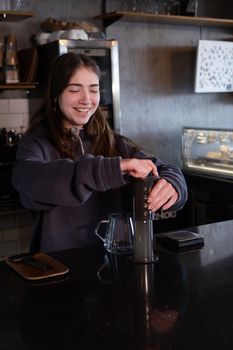 pretty brunette girl making aeropress coffee in modern coffee shop.