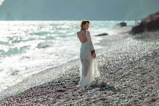 Middle aged woman looks good with blond hair, boho style in white long dress on the beach decorations on her neck and arms