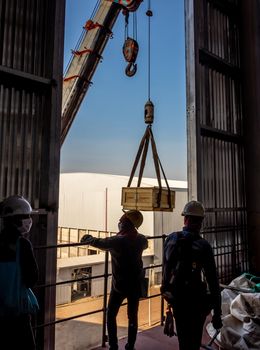 The crane carrying a wooden box of the radioactivity holder into the window on the factory floor