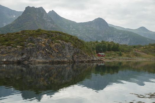Norwegian seascape, wild hut by the sea, rocky coast with dramatic skies, the sun breaks through the clouds, sheer cliffs, small islands illuminated by the sun. High quality photo
