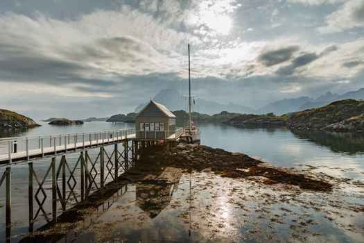 yacht boat stands at the pier against the backdrop of a picturesque mountain range, Norwegian seascape, rocky coast with dramatic skies, the sun breaks through the clouds, sheer cliffs. High quality photo
