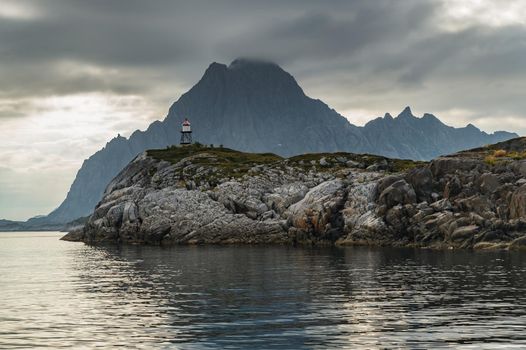 Norwegian seascape, lighthouse on the island, rocky coast with dramatic skies, the sun breaks through the clouds, sheer cliffs, small islands illuminated by the sun. High quality photo