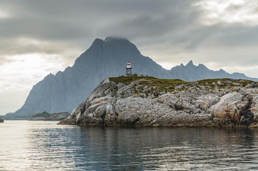 Norwegian seascape, lighthouse on the island, rocky coast with dramatic skies, the sun breaks through the clouds, sheer cliffs, small islands illuminated by the sun. High quality photo