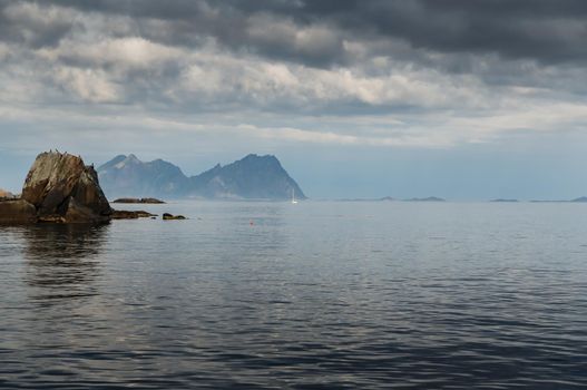 sailing yacht is on the horizon, norwegian seascape, rocky coast with dramatic skies, the sun breaks through the clouds, sheer cliffs, small islands illuminated by the sun. High quality photo
