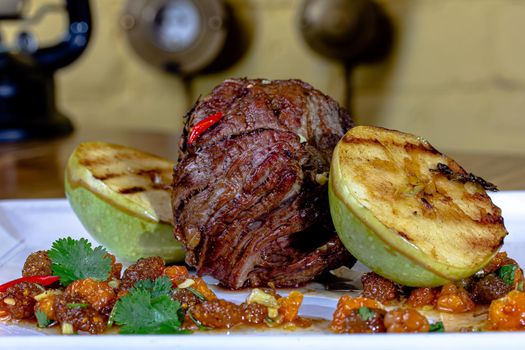 meat savory : beef fillet mignon grilled and garnished with baked apples and tomatoes on white plate isolated over white background