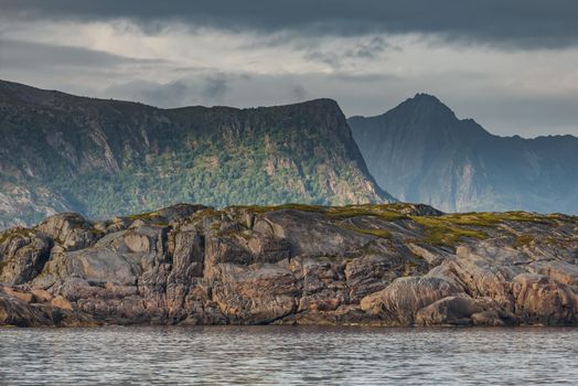 Norwegian seascape, rocky coast with dramatic skies, the sun breaks through the clouds, sheer cliffs, small islands illuminated by the sun. High quality photo