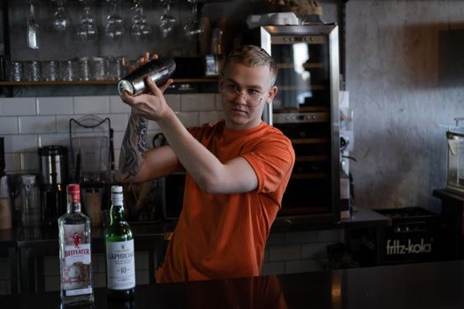 Barman is making cocktail at night club. stylish young man mixing a cocktail in a dark loft cafe. alcohol drink in modern bar. male bartender.