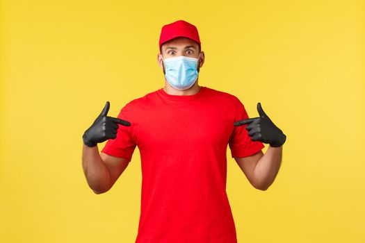 Express delivery during pandemic, covid-19, safe shipping, online shopping concept. Surprised and speechless courier in medical mask and red uniform pointing himself, being picked or chosen.