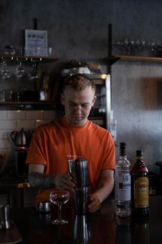 Barman is making cocktail at night club. stylish young man mixing a cocktail in a dark loft cafe. alcohol drink in modern bar. male bartender.