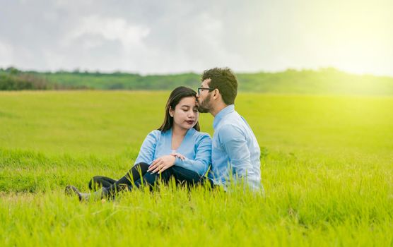 A couple in love sitting in the field kissing their foreheads, A man kissing his girlfriend's forehead in the field, Romantic couple sitting in the grass kissing their foreheads