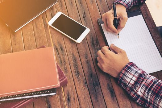 Businessman working on a desk. Freelance work at home office. Writing note on a book. Time racing. Clock ticking. Soft focus.
