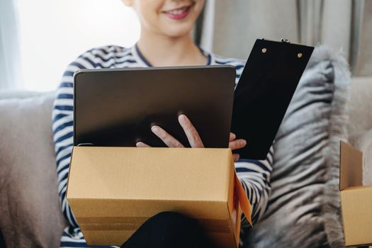 Online merchandising business idea, beautiful girl using ipad to check orders to deliver parcels to customers according to orders received from customers