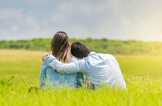 A couple in love sitting on the grass hugging from the back, a romantic couple sitting on the grass hugging from the back, rear view of a couple in love hugging on the grass