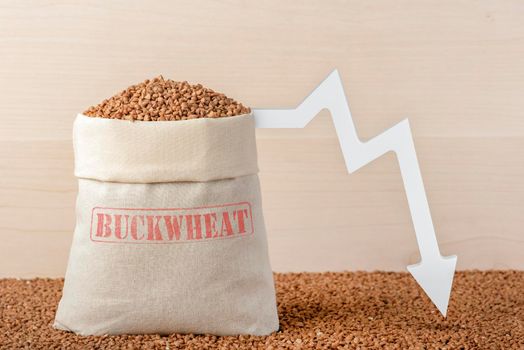 Buckwheat harvest. Poor agricultural harvests, food shortages, world hunger. A bag of buckwheat on a brown background with a white down arrow