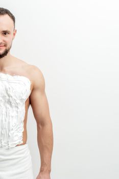 Young caucasian man with beard holds razor shaves his chest with white shaving foam on white background. Man shaving his torso